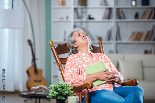 Asian Indian handsome woman with grey hair enjoy reading book at home or taking a nap on rocking chair
