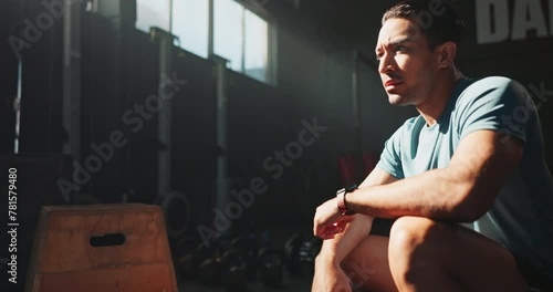 Break, exercise and time with sports man in gym to rest for recovery from training or workout fatigue. Fitness, health and watch with tired young athlete sitting to relax in performance center photo