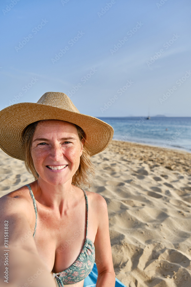 A Middle-aged woman with is taking a selfie at the beach with her smartphone