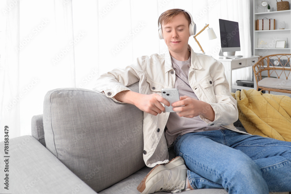 Young man in headphones using mobile phone on sofa at home