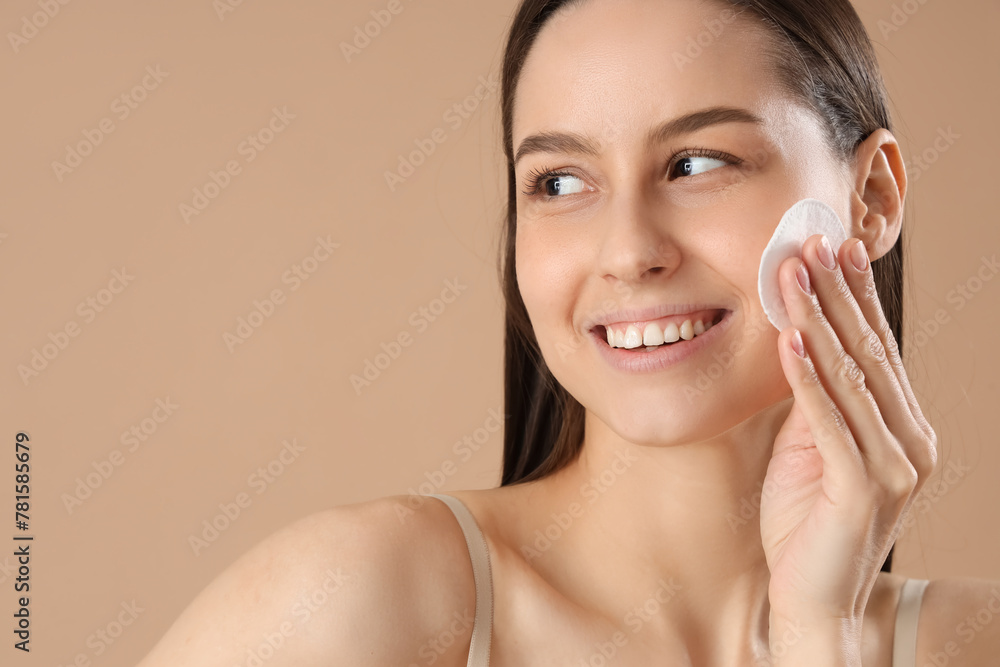 Young woman with cotton pad removing makeup on brown background, closeup