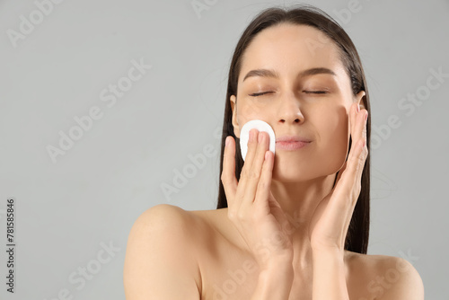 Young woman with cotton pad removing makeup on grey background, closeup