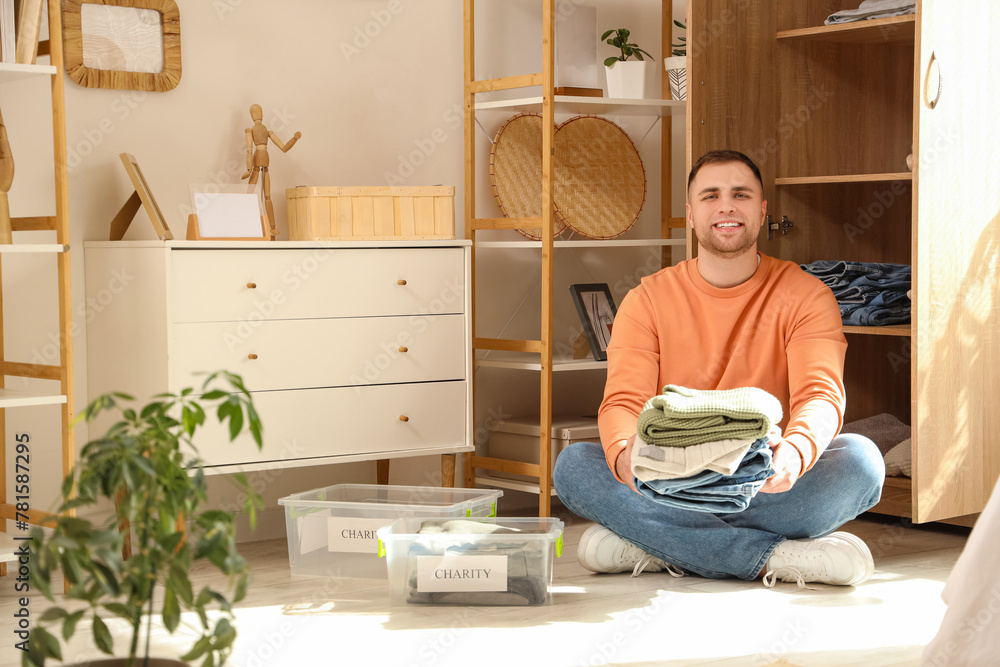 Young man with stack of charity clothes sitting at home - obrazy, fototapety, plakaty 