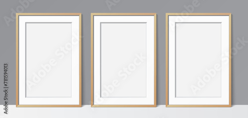 3 Blanck poster wooden frames leaning against a grey wall background. Poster gallery vector mockup for art, image, or text placement.