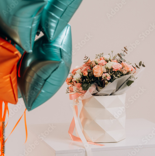 Beautiful bouquet of roses with star shaped balloons near white wall. Valentine's Day celebration