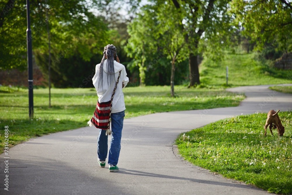 a woman with an authentic folk style bag walks with her dog in the park