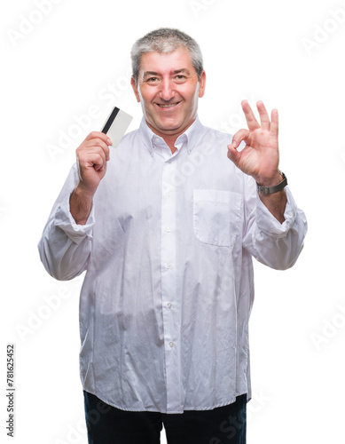 Handsome senior man holding credit card over isolated background doing ok sign with fingers, excellent symbol