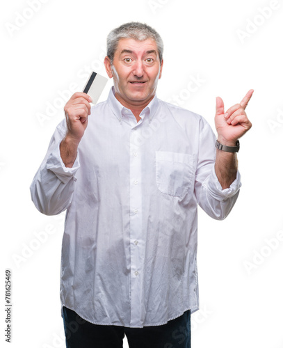 Handsome senior man holding credit card over isolated background very happy pointing with hand and finger to the side