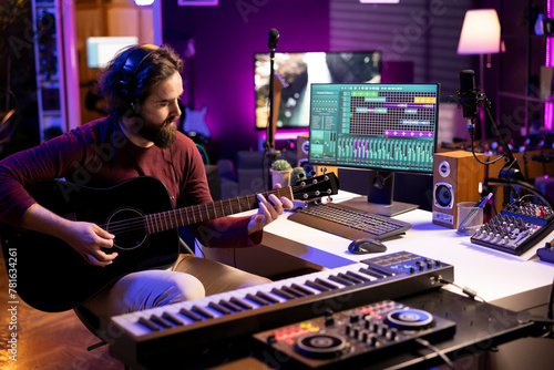 Photos Young singer playing acoustic guitar and creating music with electronic tools in home studio, using daw software interface on pc