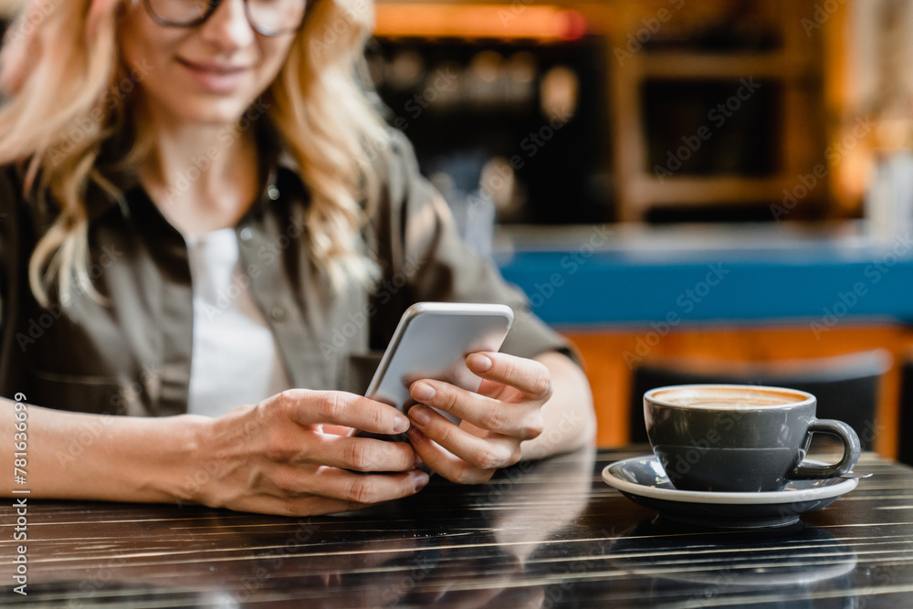 Focused cropped closeup shot of a caucasian young woman holding using smart phone cellphone for e-banking remote work while drinking coffee in cafe restaurant Focused cropped closeup shot of a caucasian young woman holding using smart phone cellphone for e-banking remote work while drinking coffee in cafe restaurant