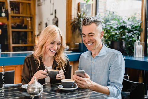 Love and relationship. Happy romantic mature couple drinking coffee in cafe restaurant on a date while husband showing his wife something on smart phone.
