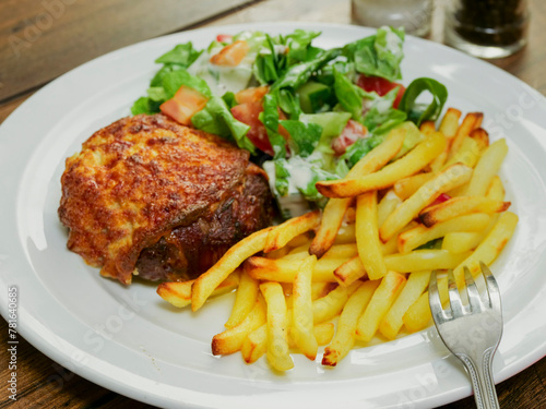 Burger with melted cheese toping, fresh green salad with lettuce and tomato and cucumber and fired potato chips on a wooden table. Tasty dinner. High quality product meal. Close up.