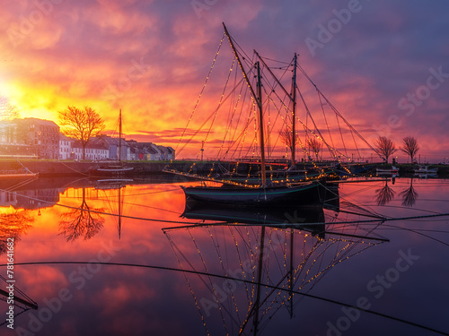 Stunning sunset scene over city buildings with reflection in water. Claddagh, docks area, Galway city, Ireland. Rich saturated colors. City center landmark area. Wooden boats in dock. photo