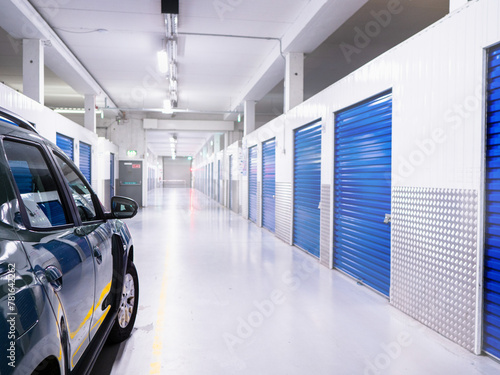 Car parked inside self storage facility with blue metal doors. Selective focus. Light and airy look. Nobody. Keeping personal items in safe dry place. Service for private and business.