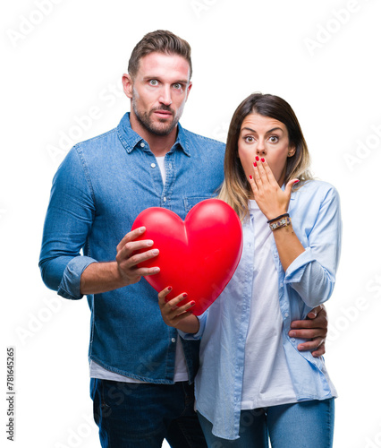 Young couple in love holding red heart over isolated background cover mouth with hand shocked with shame for mistake, expression of fear, scared in silence, secret concept