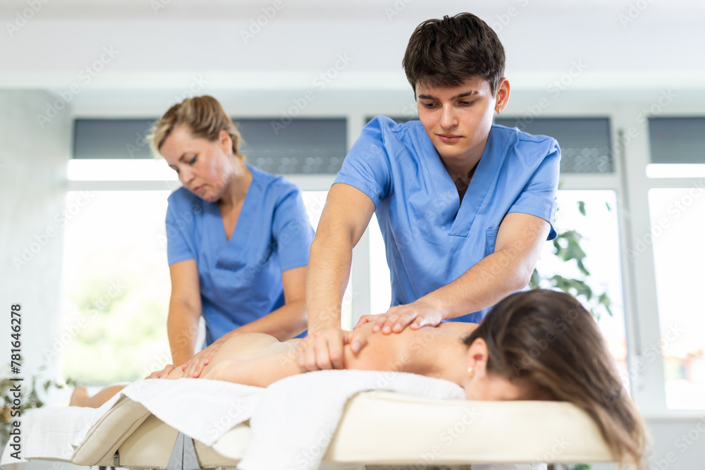 Professional masseur and masseuse performing back massage for female patient in therapy cabinet