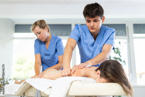 Professional masseur and masseuse performing back massage for female patient in therapy cabinet