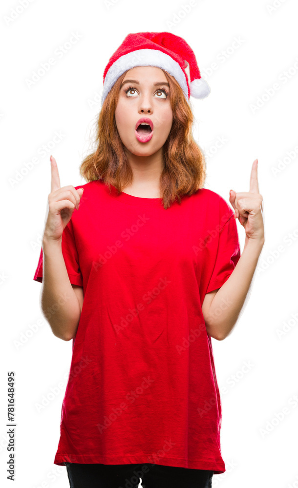 Young beautiful woman over isolated background wearing christmas hat amazed and surprised looking up and pointing with fingers and raised arms. Young beautiful woman over isolated background wearing christmas hat amazed and surprised looking up and pointing with fingers and raised arms.