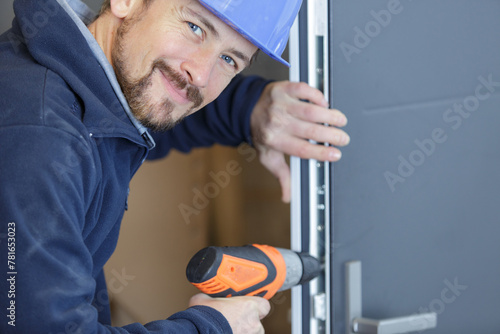 happy male worker drills a hole in a door