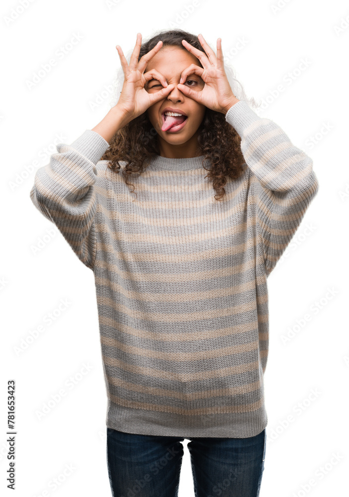 Beautiful young hispanic woman wearing stripes sweater doing ok gesture like binoculars sticking tongue out, eyes looking through fingers. Crazy expression. Beautiful young hispanic woman wearing stripes sweater doing ok gesture like binoculars sticking tongue out, eyes looking through fingers. Crazy expression.