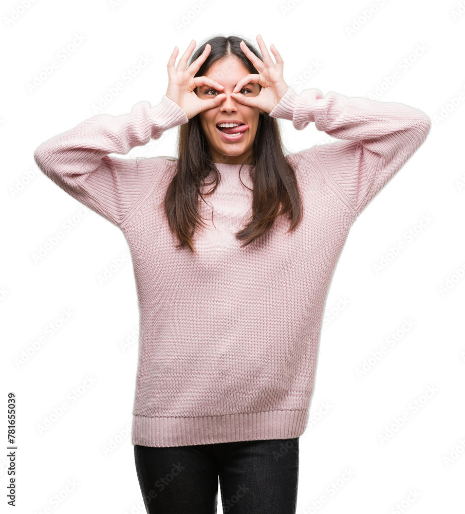 Young beautiful hispanic woman wearing a sweater doing ok gesture like binoculars sticking tongue out, eyes looking through fingers. Crazy expression. Young beautiful hispanic woman wearing a sweater doing ok gesture like binoculars sticking tongue out, eyes looking through fingers. Crazy expression.