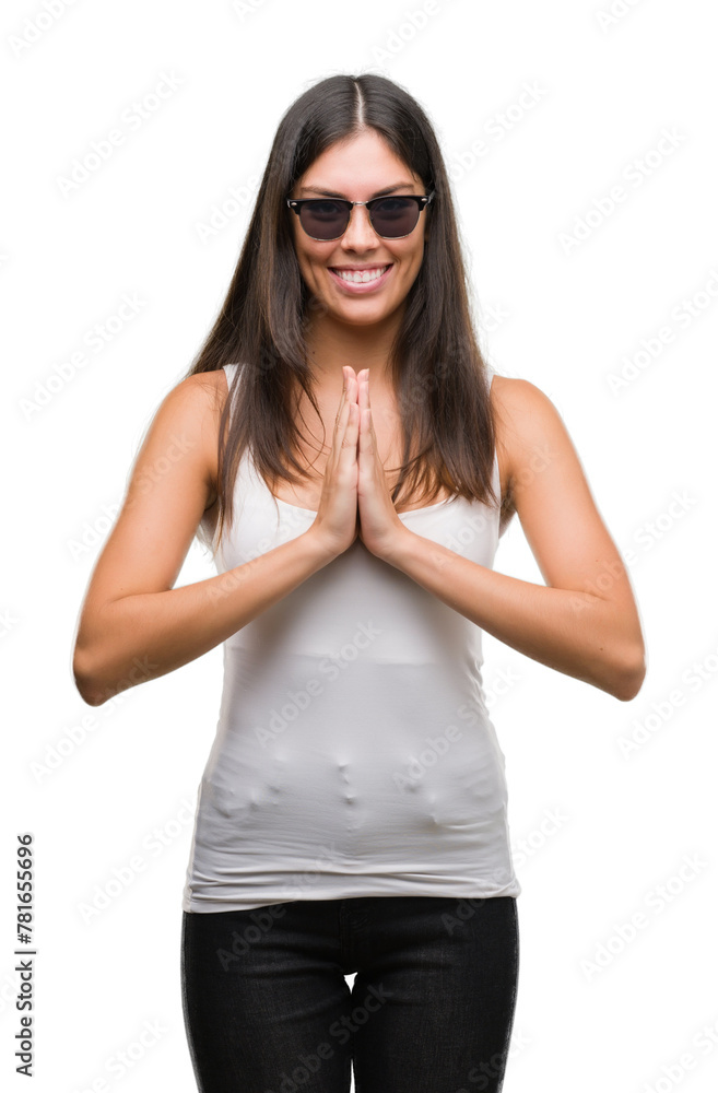 Young beautiful hispanic wearing sunglasses praying with hands together asking for forgiveness smiling confident. Young beautiful hispanic wearing sunglasses praying with hands together asking for forgiveness smiling confident.