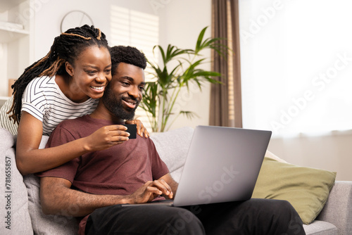 Joyful African American couple using a credit card to shop online, sitting comfortably on the couch at home. photo