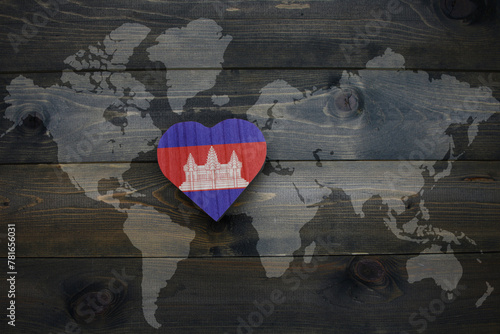 wooden heart with national flag of cambodia near world map on the wooden background.