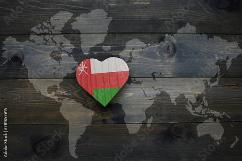 wooden heart with national flag of oman near world map on the wooden background.