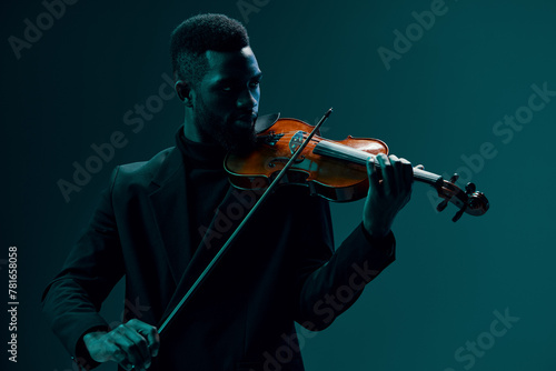 Elegant man in black suit playing the violin on dark background in atmospheric setting photo