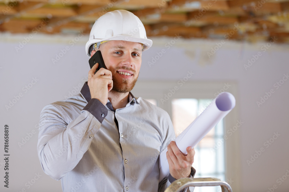 male architect holding rolled up plans and talking on telephone - obrazy, fototapety, plakaty 