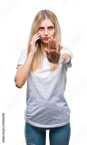 Young beautiful blonde woman talking using smartphone over isolated background with open hand doing stop sign with serious and confident expression, defense gesture © Krakenimages.com