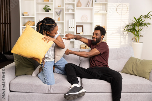 A Happy Young Couple Engages In a Playful Pillow Fight on Their Cozy Living Room Couch, Radiating Joy And Togetherness.