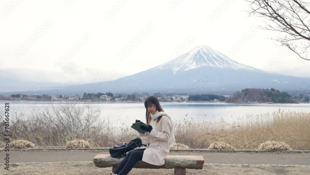 Happy Asian woman working on digital tablet with internet by Kawaguchi lake with mount Fuji covered in snow background. Attractive girl enjoy outdoor lifestyle travel nature and famous place in Japan. Happy Asian woman working on digital tablet with internet by Kawaguchi lake with mount Fuji covered in snow background. Attractive girl enjoy outdoor lifestyle travel nature and famous place in Japan.