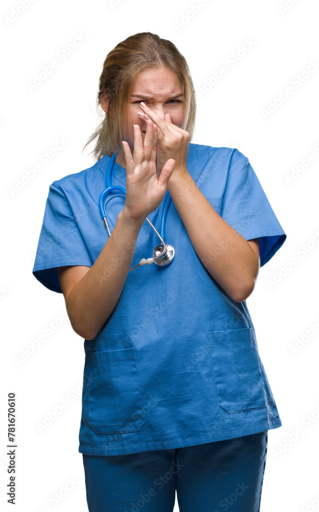 Young caucasian doctor woman wearing surgeon uniform over isolated background smelling something stinky and disgusting, intolerable smell, holding breath with fingers on nose. Bad smells concept.