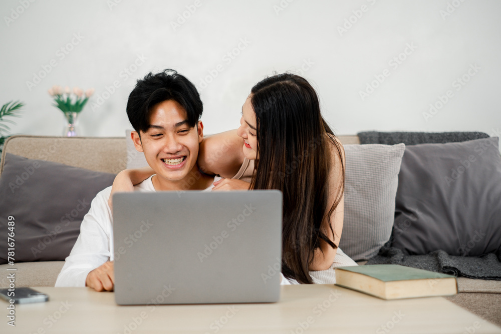 Young couple is sharing a cheerful moment on a couch with a laptop. The man, dressed in a white shirt, laughs while the woman, in a sleeveless top, leans in with an affectionate smile. Young couple is sharing a cheerful moment on a couch with a laptop. The man, dressed in a white shirt, laughs while the woman, in a sleeveless top, leans in with an affectionate smile.