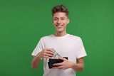 Happy man putting money into his wallet on green background
