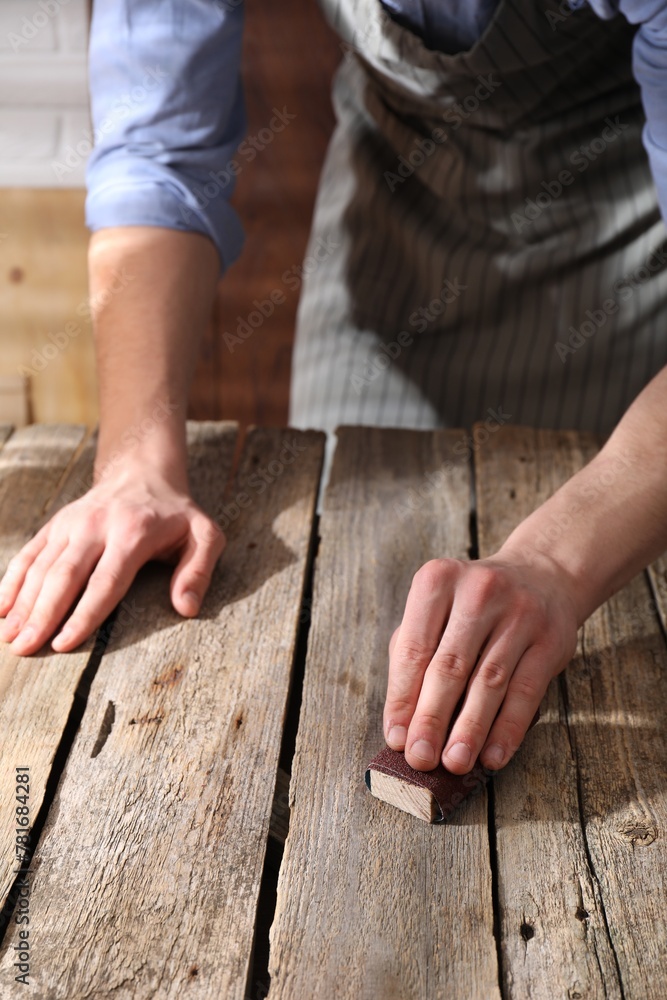 Man polishing wooden table with sandpaper indoors, closeup Man polishing wooden table with sandpaper indoors, closeup