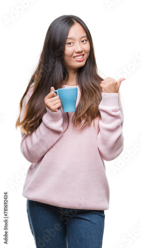 Young asian woman drinking coffee over isolated background pointing and showing with thumb up to the side with happy face smiling