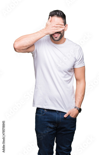 Young man wearing casual white t-shirt over isolated background smiling and laughing with hand on face covering eyes for surprise. Blind concept.