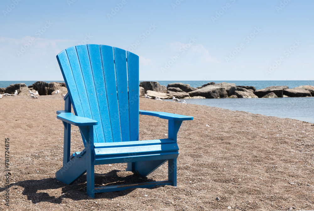 blue wooden beach chair on the sand near the ocean with a blue sky
