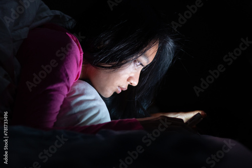 A young woman is lying in bed and using a smart phone