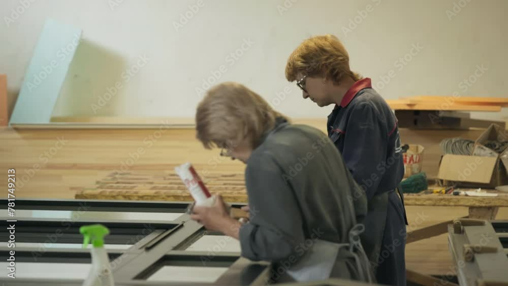 Carpenters Work On Wooden Window Improvement In Production Workshop. Workshop Carpenters Producing Window By Applying SIlicon Gel On Glass. Female Carpenters. Woodworking Workshop. Window Production Carpenters Work On Wooden Window Improvement In Production Workshop. Workshop Carpenters Producing Window By Applying SIlicon Gel On Glass. Female Carpenters. Woodworking Workshop. Window Production