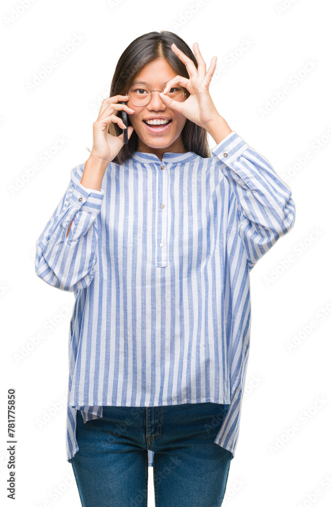 Young asian woman speaking on the phone over isolated background with happy face smiling doing ok sign with hand on eye looking through fingers Young asian woman speaking on the phone over isolated background with happy face smiling doing ok sign with hand on eye looking through fingers