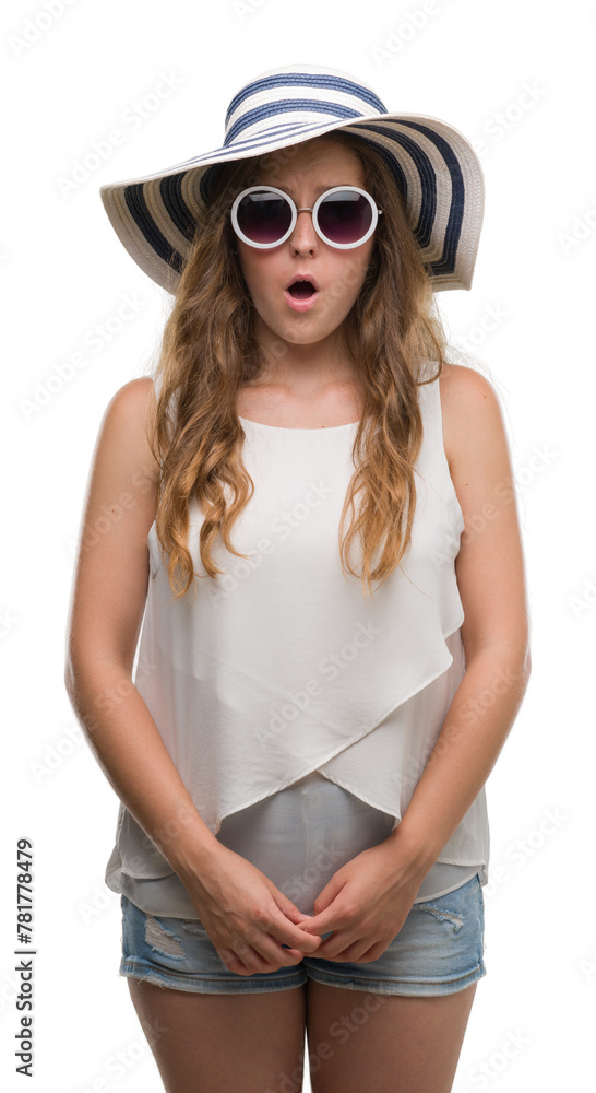 Young blonde woman wearing sunglasses and summer hat scared in shock with a surprise face, afraid and excited with fear expression Young blonde woman wearing sunglasses and summer hat scared in shock with a surprise face, afraid and excited with fear expression