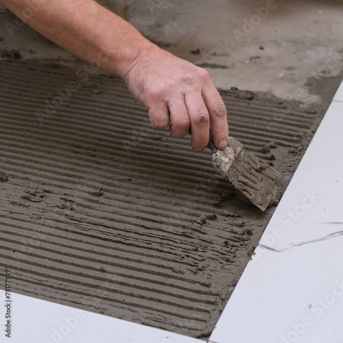 Construction worker applies cement for laying floor ceramic tiles with spatula