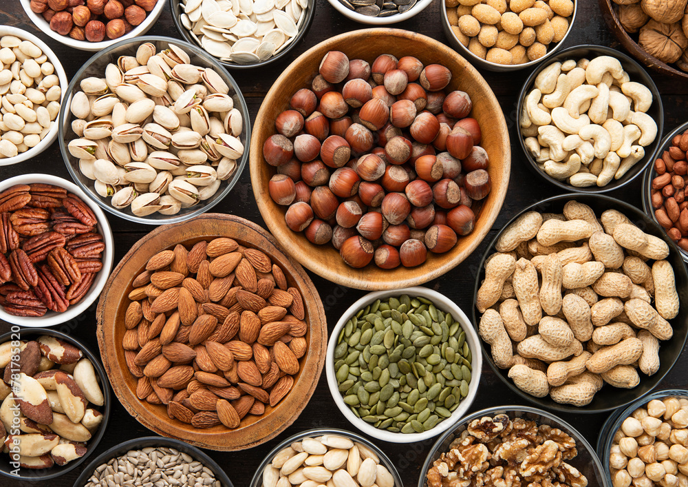 Mixed healthy nuts and seeds in various bowls on dark kitchen table.Peanut,hazelnut,walnut,almonds,pistachio,sunflower,pumpkin,chia and cashew.Top view.