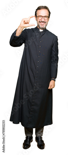 Middle age priest man wearing catholic robe smiling and confident gesturing with hand doing size sign with fingers while looking and the camera. Measure concept.