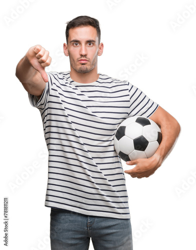 Handsome young man holding soccer football with angry face, negative sign showing dislike with thumbs down, rejection concept
