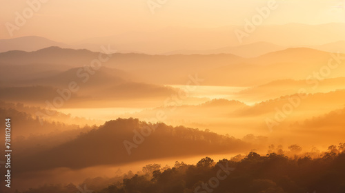 The warm golden rays of the sunrise bathe a mystic mist-covered mountain range in vivid light